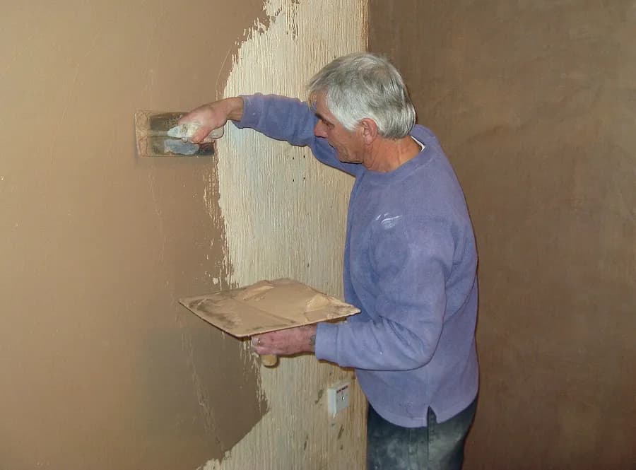 Ein Stuckateur trägt die Glättlage einer Innenwand auf, mit Glättkelle und Putzbrett. Ein Stuckateur trägt die Glättlage einer Innenwand auf, mit Glättkelle und Putzbrett.